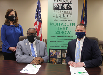 Caucasian male wearing a blue face mask, blue suit jacket, white collared shirt, light blue tie, hands folded while sitting down at a table, white paper in front of him with a green pen; African American male wearing a black Augusta Tech branded face mask, light gray suit, silver Augusta Tech lapel pin, white collared shirt, blue/purple tie, silver watch, hands folded white sitting at a brown table, white papers on brown table in front of him with a green pen; Caucasian female standing wearing a black Augusta Tech branded face mask, blue shirt, hands folded together, black pants, background features an American flag, the state of Georgia flag, large retractable banner showing old Augusta Tech logo, verbiage reads: pfi.4dian8.com, Education That Works; bulleted list reads Allied Health Sciences and Nursing, Business and Personal Services, and Engineering Technology, Industrial Technology, and Learning Support, photos underneath the bulleted list.